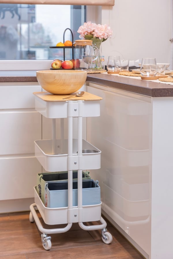 White rolling storage cart with wooden bowl in modern kitchen.