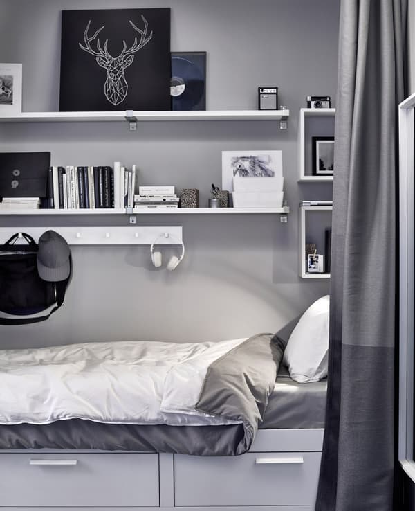 White shelving and hooks store artwork, books, boxes and more above a small bed area.