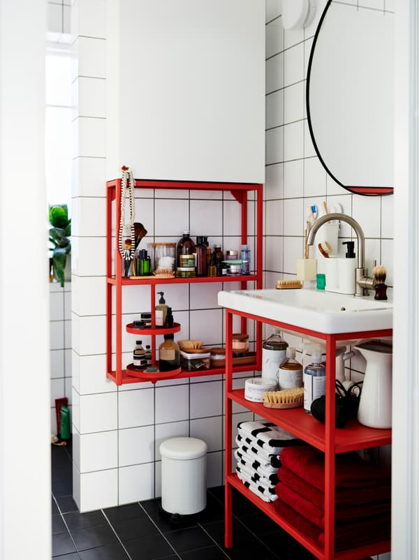 White-tiled bathroom furnished with a mix of red and white ENHET modules, holding decorations and accessories.