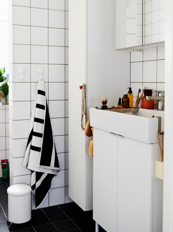White-tiled bathroom furnished with white LILLÅNGEN cabinets and washbasin, and dotted with decorations and accessories.