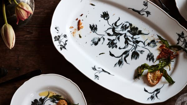 White UPPLAGA serving and side plates with a floral pattern, holding leftover food, placed on a wooden table with tulips.