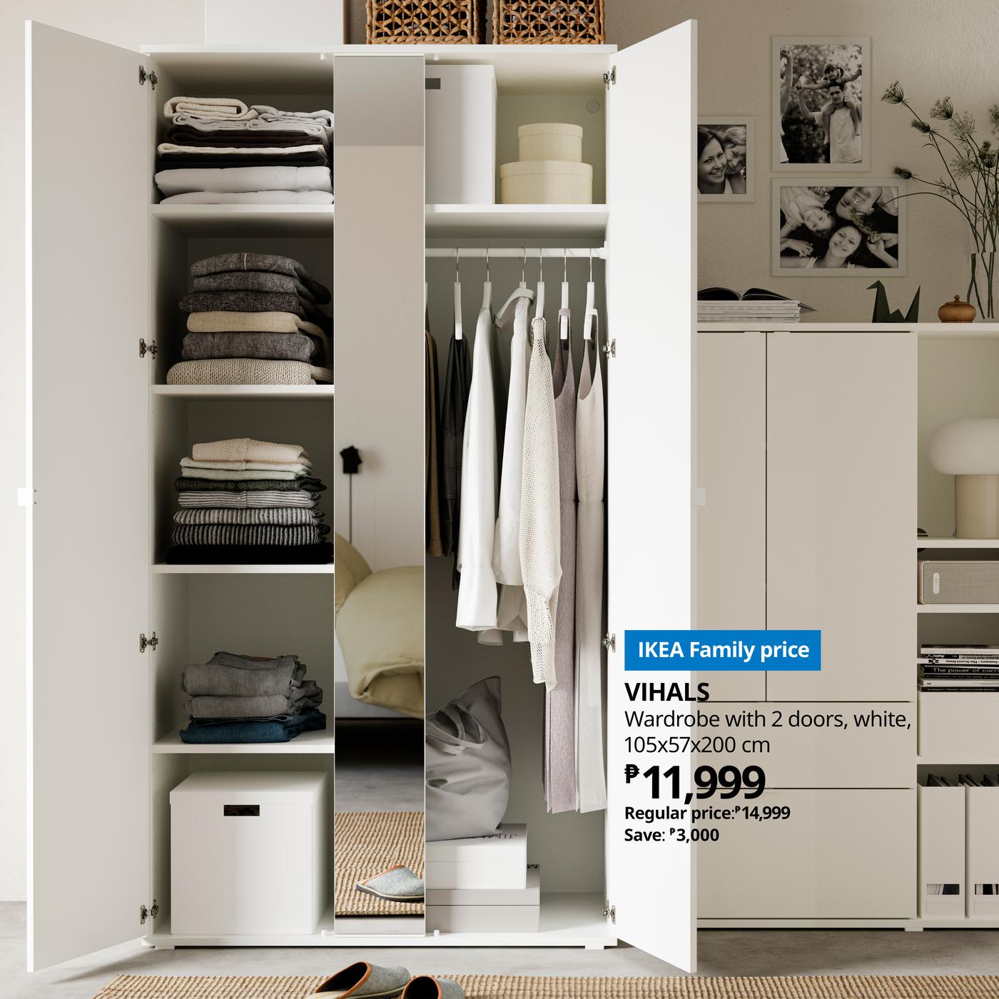White wardrobe with open doors displaying folded clothes and hanging garments. Label shows IKEA family price of ₱11,999. Cozy and organized setting.