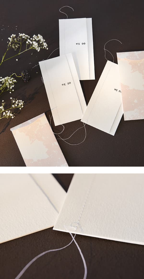 White wedding invitations are given a personal touch with stamps and a threaded seam.