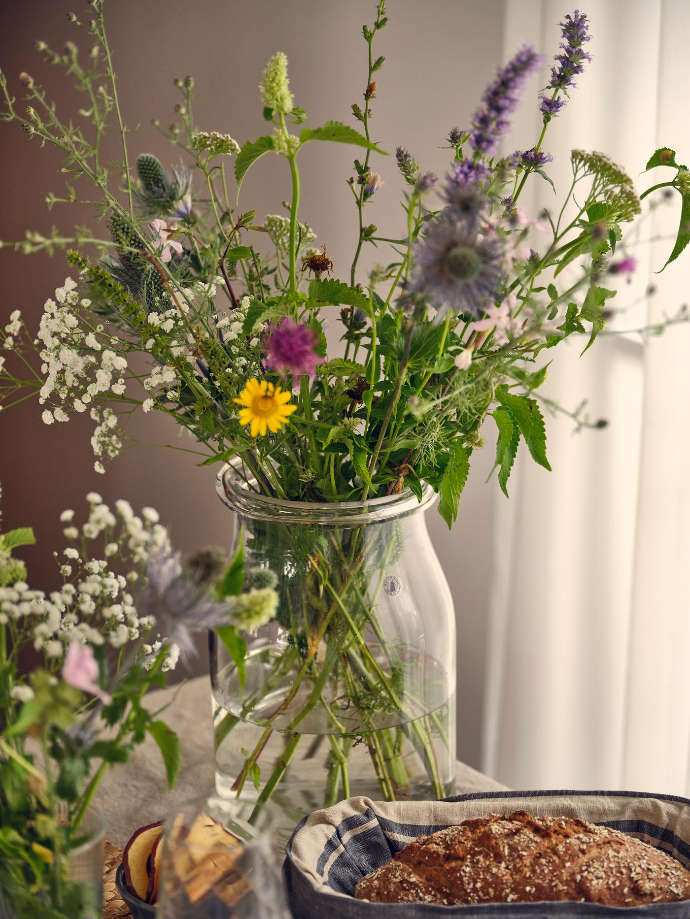 Wildflower bouquet in a glass vase on a set table with bread and napkin in a natural summer style.