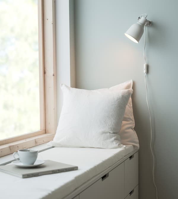 Window seating in a bedroom made of white NORDLI chest of drawers, two white cushions and a thin mattress pad.