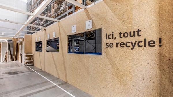 Winkelruimte met hergebruikbalie en opschriften over recyclage, ingebouwd in wanden van houtachtig materiaal.