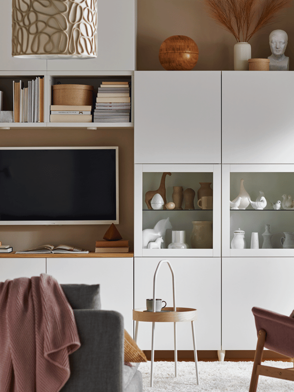 Witte BESTÅ kasten met gesloten deurtjes en twee glazen deurtjes en daarvoor staat een bijzettafel