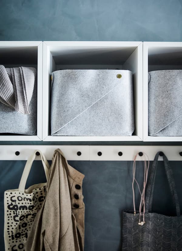 Witte IKEA EKET open kastjes met daarin vilten opbergers; daaronder hangen draagtassen aan haken.
