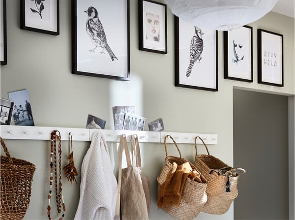 Witte kapstok met haken, zwarte fotolijsten met foto's en manden gemaakt van zeegras.