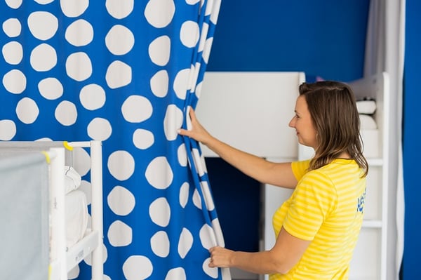 Woman adjusting blue polka dot curtain in children’s bedroom interior