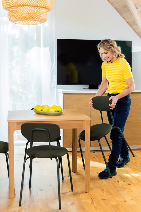 Woman arranging dining chair at wooden table in bright kitchen and dining space