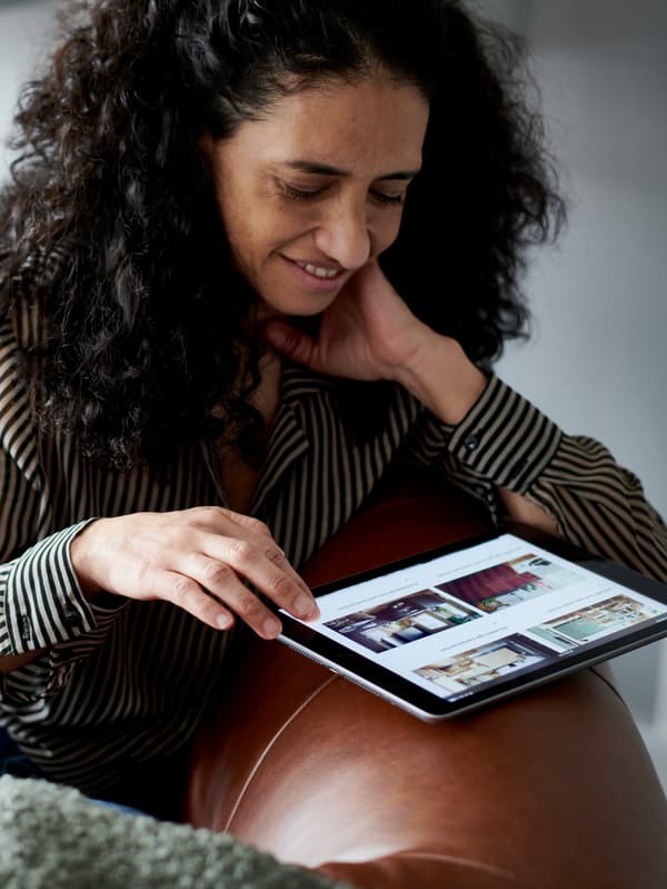 Woman browsing the IKEA website on a tablet while sitting on a brown leather sofa