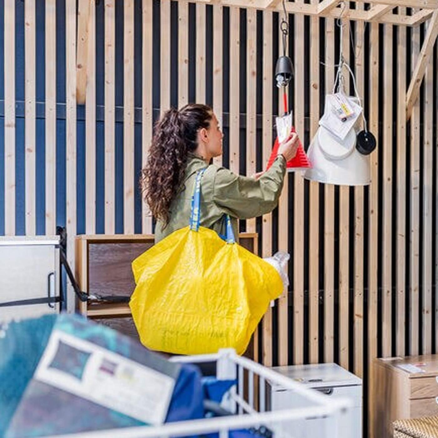 Woman carrying a yellow IKEA shopping bag browsing items for sale in the As-is department.