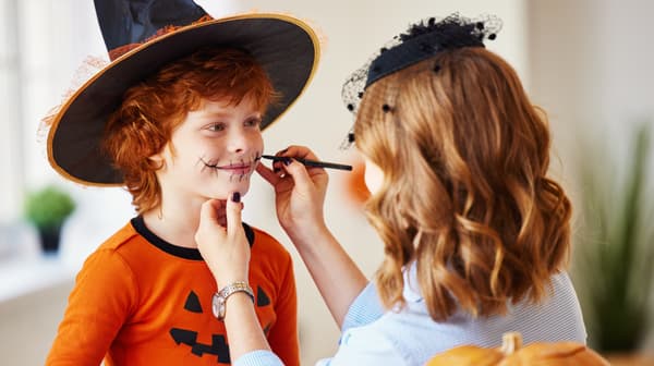 Woman doing an halloween makeup on a boy with a pumpkin costume