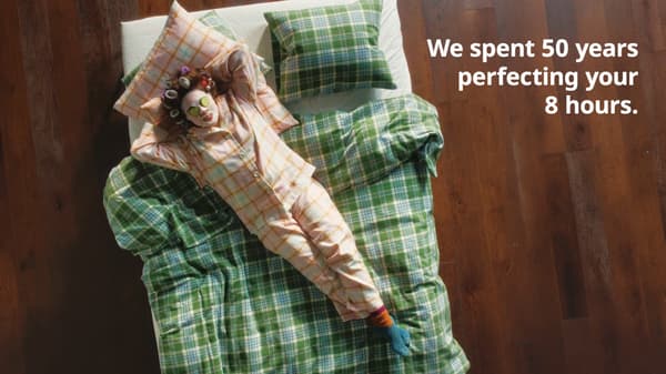 Woman in pink pyjamas doing a cucumber face mask and lazing on bed. White text on right read: We spent 50 years perfecting your 8 hours.