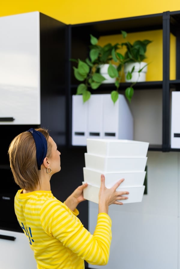 Woman organizing white storage boxes on office shelves in a modern workspace
