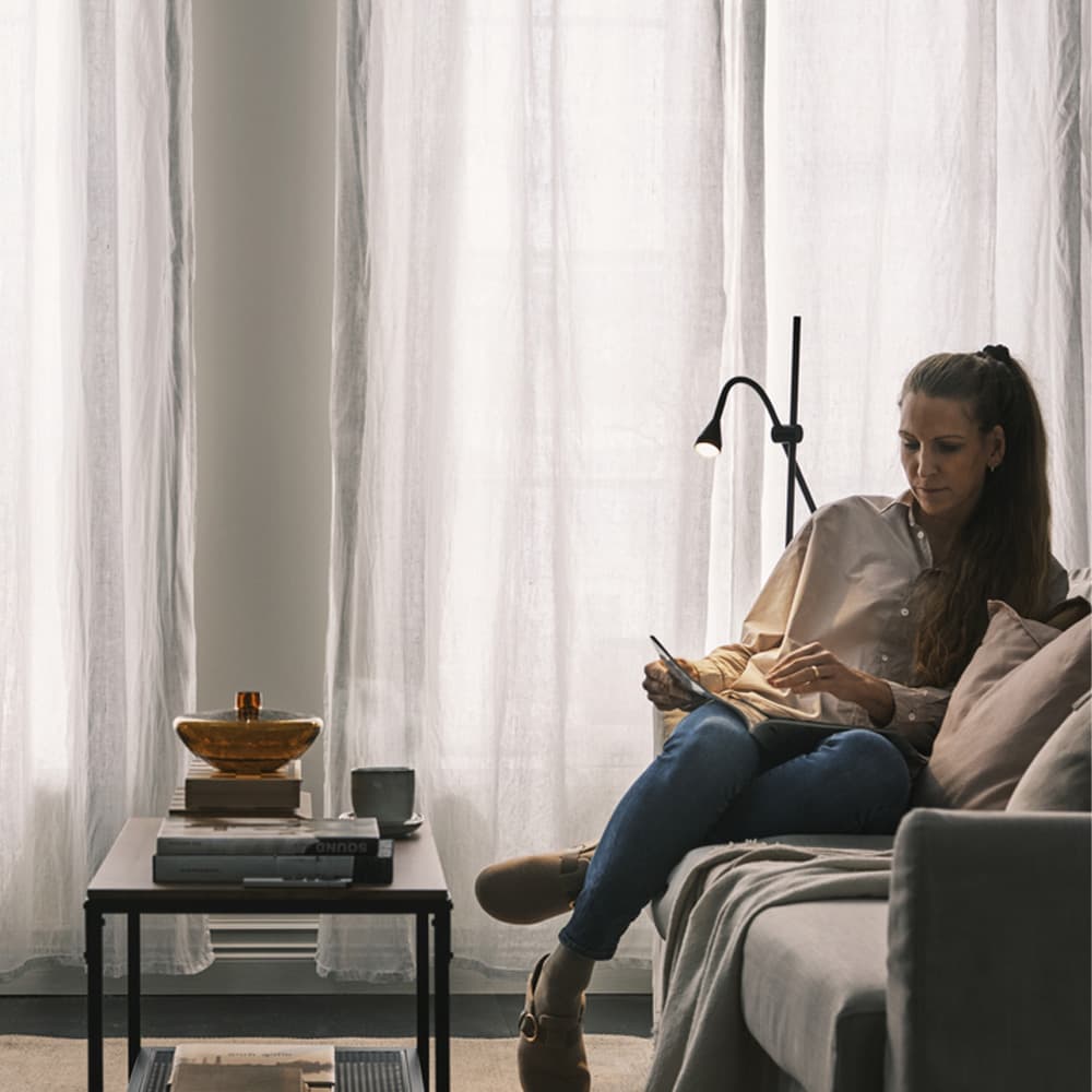 Woman reading book in living room against dimming curtains 