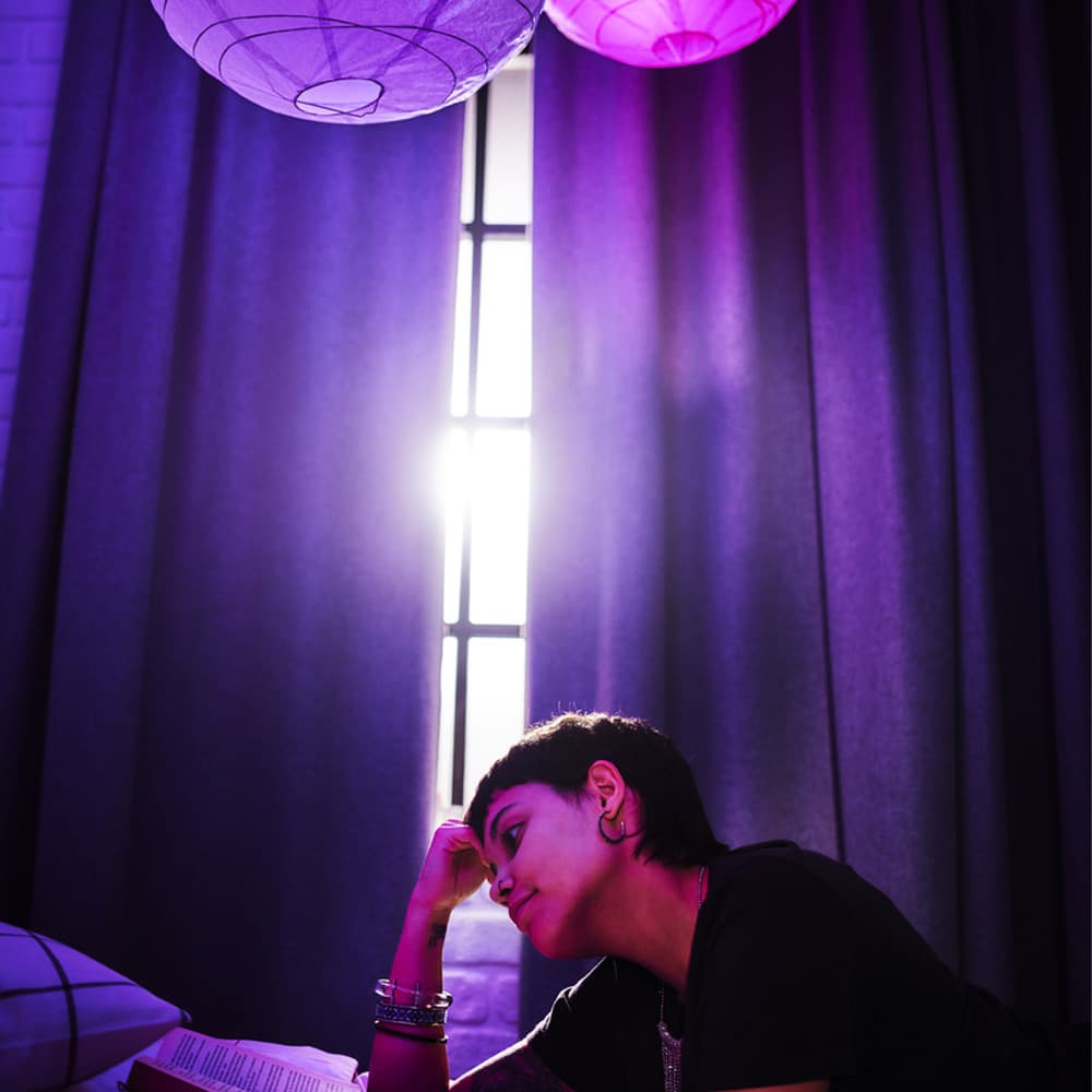 Woman reading book on bed in bedroom with IKEA room darkening curtains over the window.