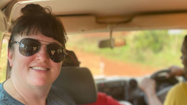 Woman seated in a moving car, with a green landscape visible through the windshield.