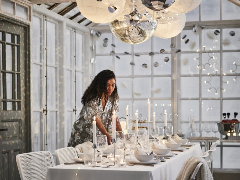 Woman setting tablescape featuring IKEA FRÖJDA collection including glasses, napkins and silverware.