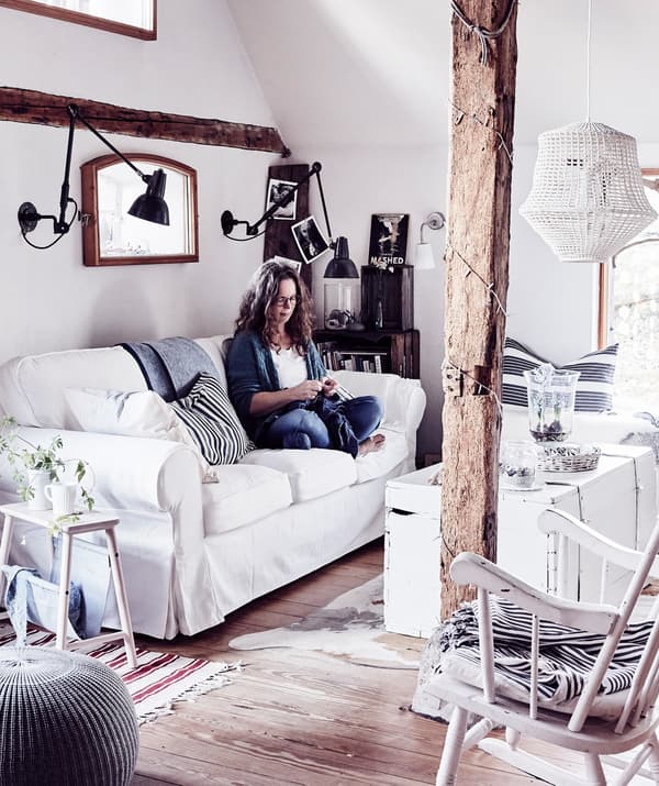 Woman sitting on a white sofa in a living room with wooden beams and floorboards.
