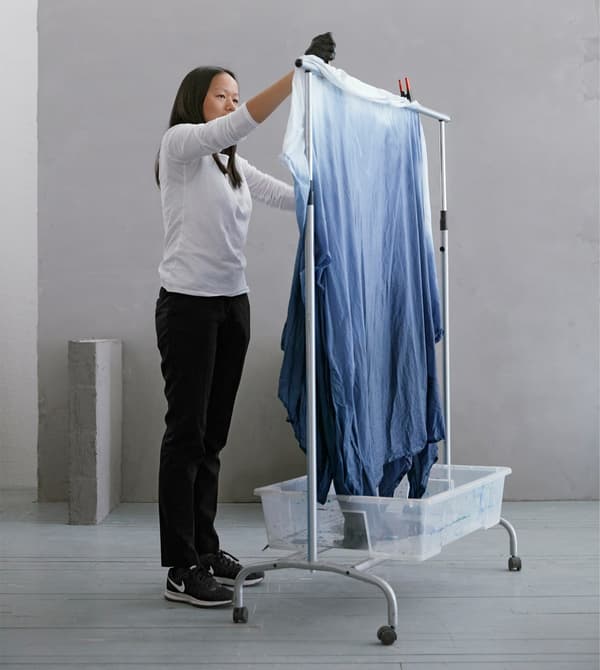 Woman standing with dyed cotton fabric BOMULL on a clothes rack as a drying rack with a plastic bin underneath to catch drips.