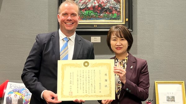 感謝状を手に並ぶ二人。富士山の絵画や表彰状が飾られたオフィスで、受賞の瞬間を記念撮影。