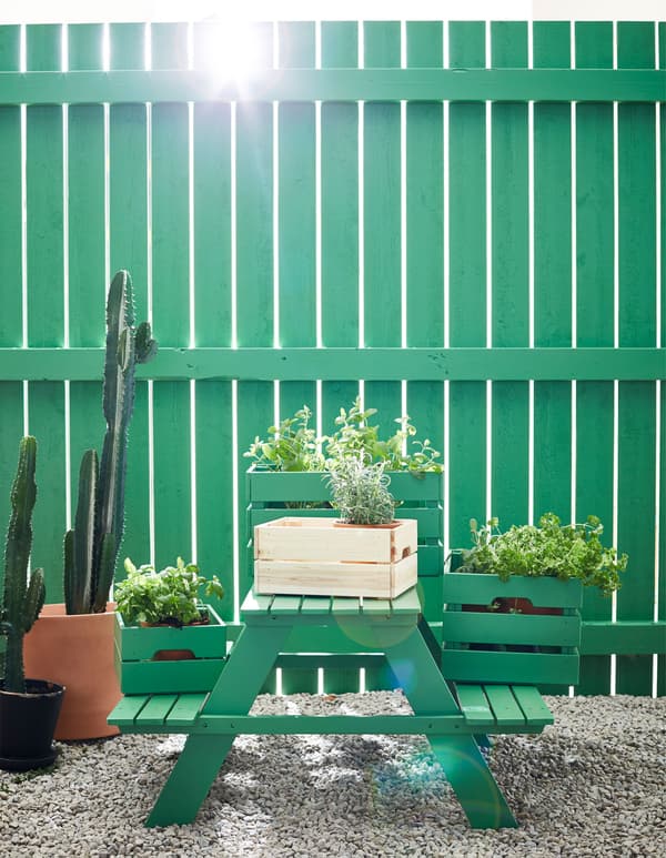 Wooden boxes are filled with potted plants and displayed on a green picnic table.
