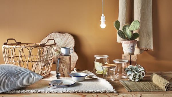 Wooden dining room table with bamboo mat, glass jars, plants and plateware.