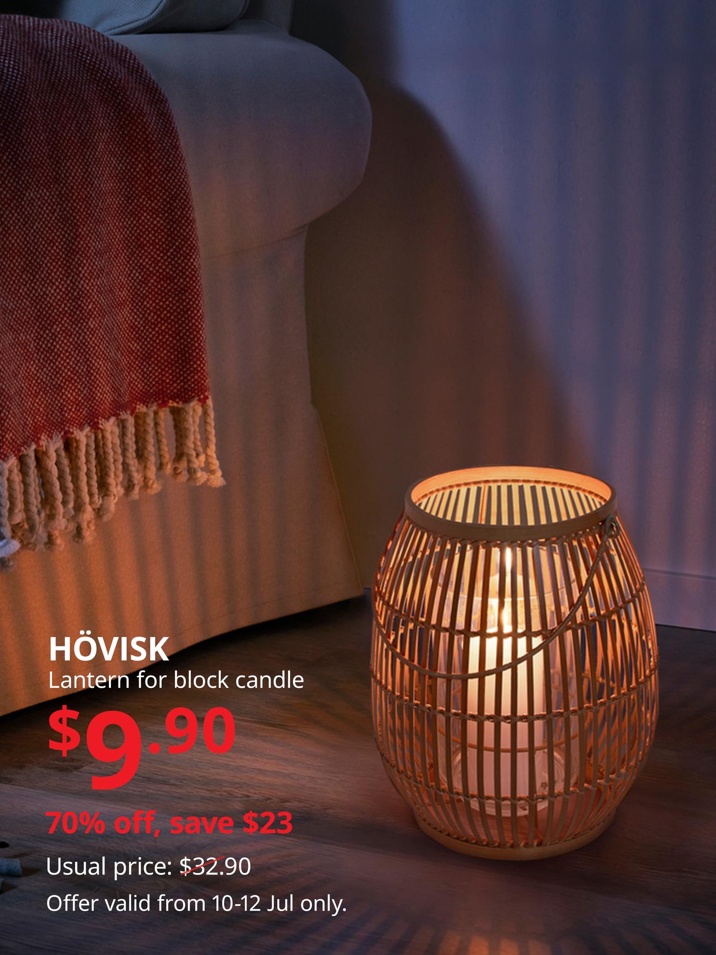 Wooden lantern with a lit candle beside a sofa draped with a warm throw blanket.