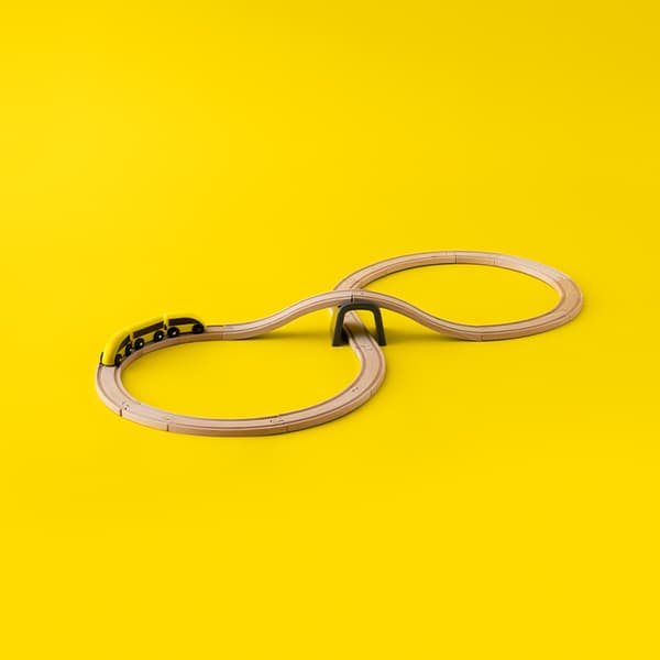 Wooden toy train set in a figure-eight layout with a small yellow train and an overpass bridge, placed on a bright yellow background.