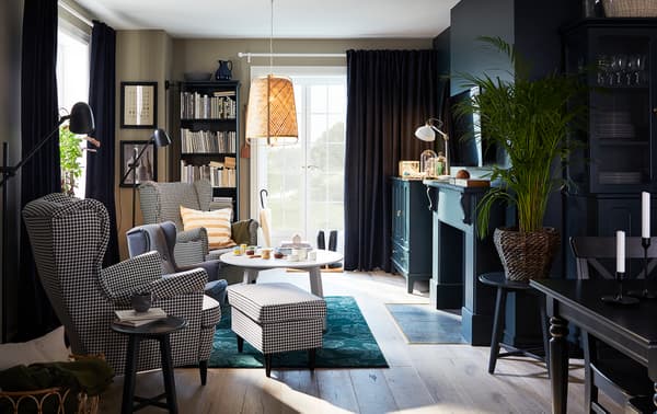 Woonkamer met twee oorfauteuils versierd met een pied-de-poule-motief, een groen vloerkleed, een hanglamp in bamboe en een ronde salontafel.