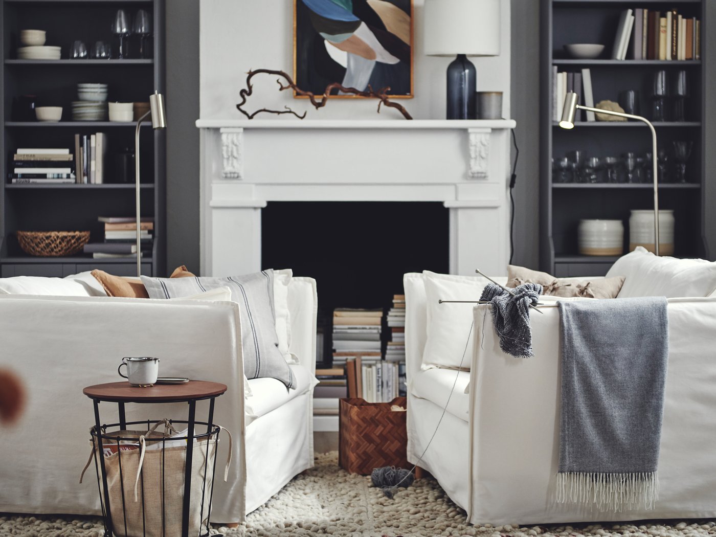 Woonkamer met twee witte BACKSÄLEN fauteuils die tegenover elkaar staan met daarachter grijze HAUGA hoge kasten rond een haard.