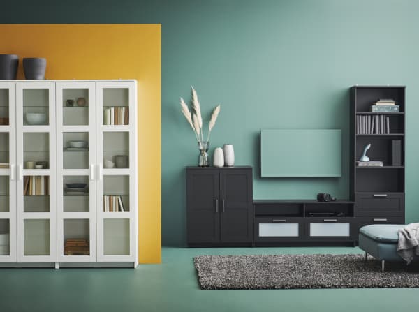 Woonkamer met witte en zwarte meubels, gele en groene muur, grijs VINDUM vloerkleed en poef.
