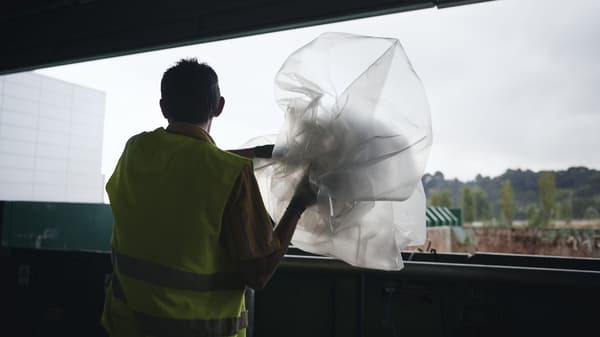 Worker in safety vest disposing large sheet of plastic at recycling facility.