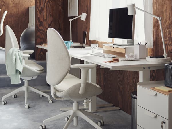 Workspaces with white TROTTEN desks and HATTEFJÄLL and LÅNGFJÄLL office chairs in a carpeted, brown, wood-panel office.