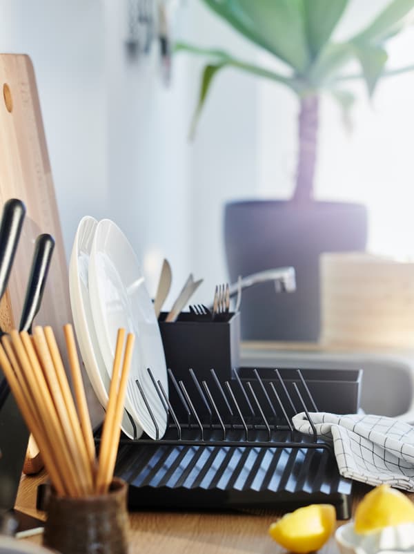 Worktop dotted with kitchen accessories including lemon halves, a cup holding chopsticks, and a black RINNIG dish drainer.