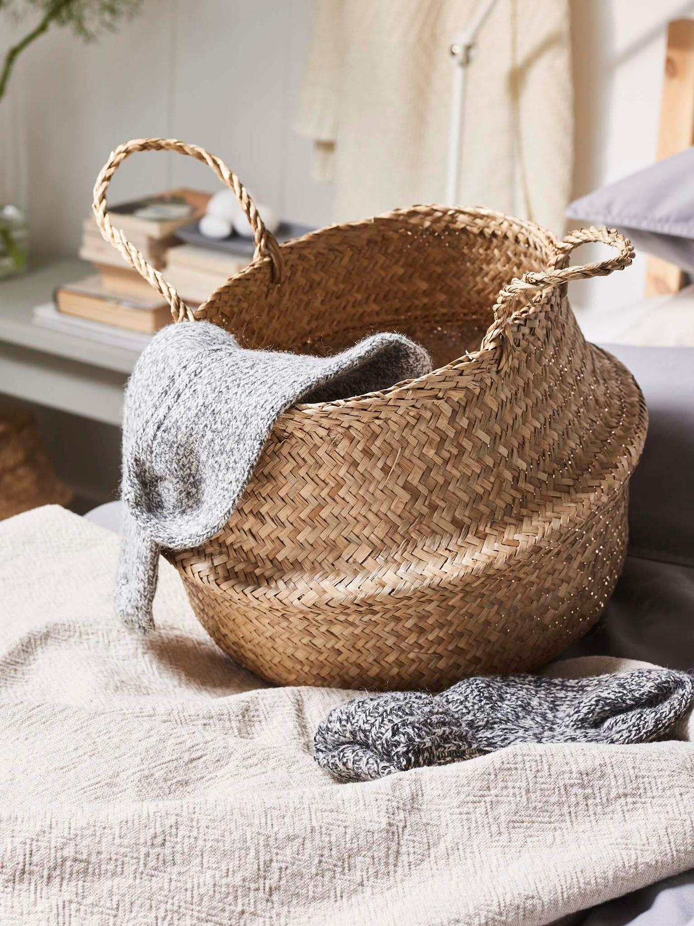 Woven FLÅDIS basket sitting on a bed in neutral colours.