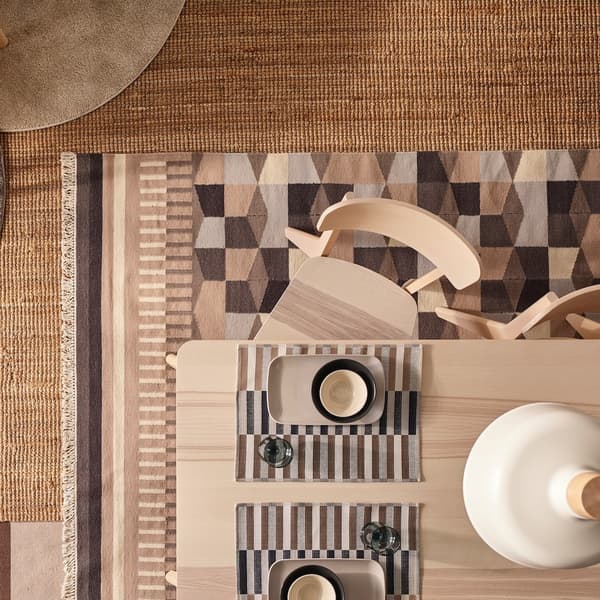 Woven rug with a geometric pattern in beige, brown and grey under a light wood dining table