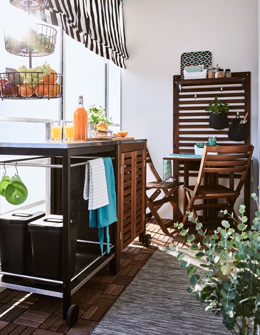 Wózek, szafka i mały stolik tworzą na balkonie przestrzeń, w której można przygotować i cieszyć się jedzeniem.