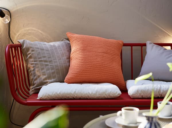 وسائد بيج وبرتقالي مقاومة للبهتان ومقاومة للماء مرتبة على كنبة خارجية BRUSEN من ايكيا ذات 3 مقاعد.