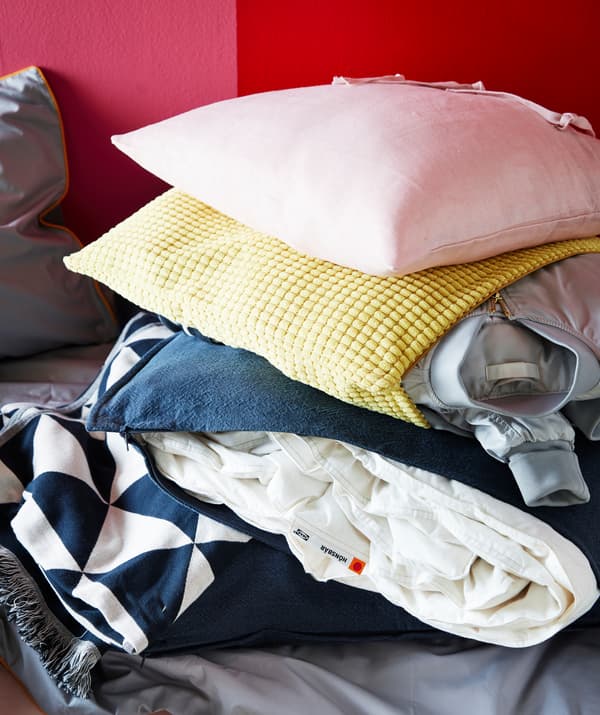 Yellow GULLKLOCKA cushion cover with a jacket inside and a blue cover used to store an off-season blanket.