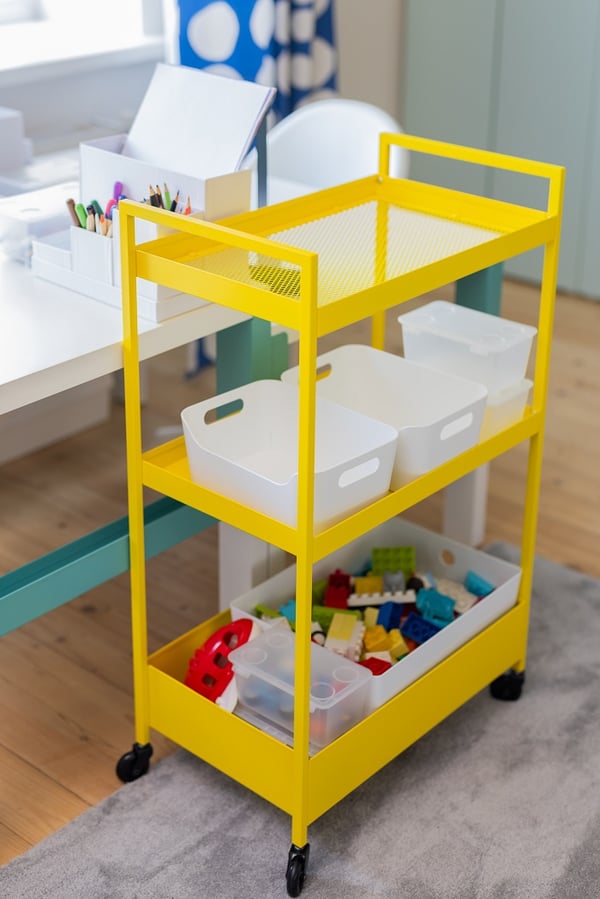 Yellow rolling storage cart with bins and toys next to children’s desk