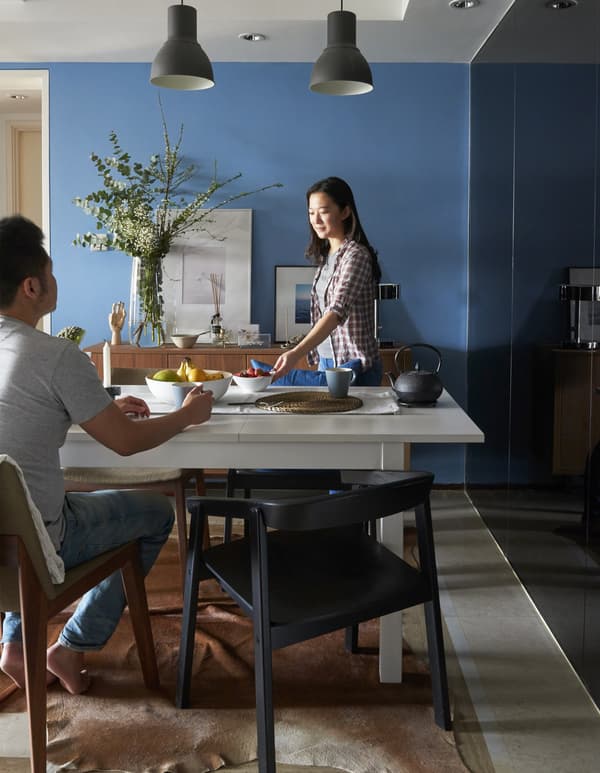 Yiqing serving food in a dining room and Derrick sitting at the table.