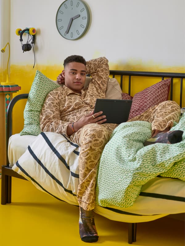 Young man using a tablet on a day bed in a yellow room.