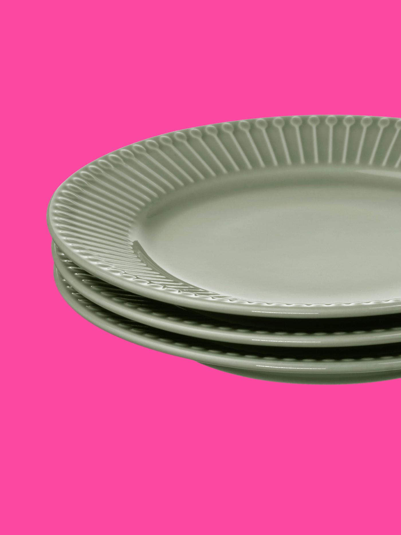 Yre gröna tallrikar staplade på varandra mot rosa bakgrund.