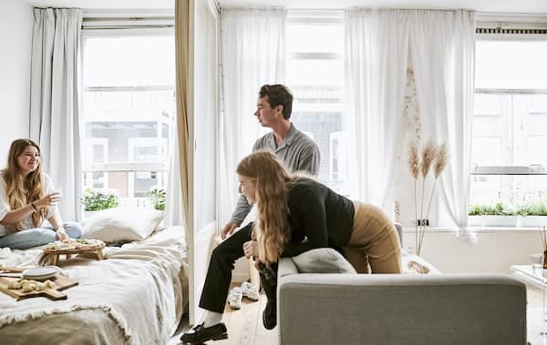 Yvet and her friends gathered on the sofa and bed  with large windows behind.
