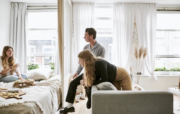 Yvet et ses amis réunis sur le canapé et le lit, avec de grandes baies vitrées derrière.