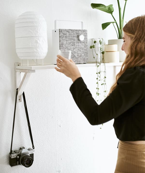 Yvet places a glass on a shelf with a lamp, speaker and plants.