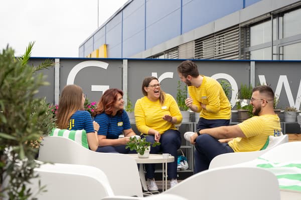 Zaměstnanec IKEA ve žluté uniformě s nápisem „Hej!“ na zadní straně košile.
